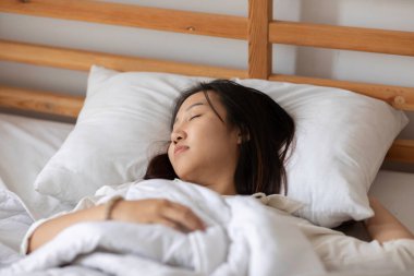 Pijama giyen güzel Asyalı kadın gözlerini kapar, gülümser ve tatlı rüyalar görür. Sabah yatak odasında rahat ve rahat hisseder. Sağlık ve Uyku Konsepti.