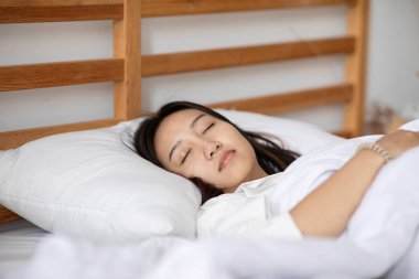 Pijama giyen güzel Asyalı kadın gözlerini kapar, gülümser ve tatlı rüyalar görür. Sabah yatak odasında rahat ve rahat hisseder. Sağlık ve Uyku Konsepti.