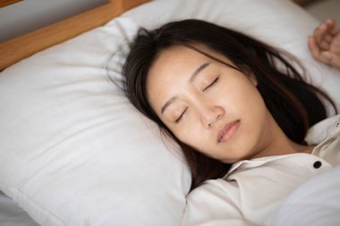 Pijama giyen güzel Asyalı kadın gözlerini kapar, gülümser ve tatlı rüyalar görür. Sabah yatak odasında rahat ve rahat hisseder. Sağlık ve Uyku Konsepti.