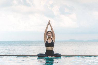 Güzel Çekici Asyalı kadının yoga nilüferinde dinlendiği tatil. Plajın yukarısındaki havuzda poz veriyor. Tropikal adada güzel bir deniz var.