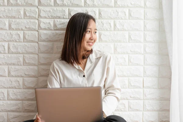 リビングルームに座っているアジアの若い女性の笑顔を離れて見て ソーシャルメディアやオンラインショッピングを使用するためのコンピュータのラップトップを使用してとても幸せと陽気な感じ — ストック写真