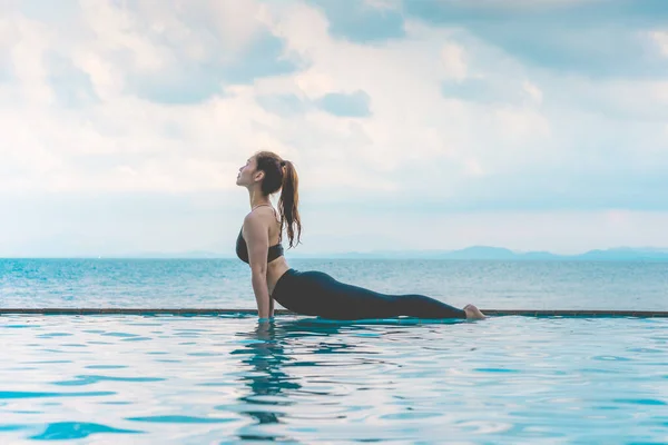 魅力的なアジアの女性の練習の休暇コブラ熱帯の島で美しい海と朝のビーチの上のプールにポーズ 休日に快適さとリラックス感 休暇のコンセプト ロイヤリティフリーのストック画像