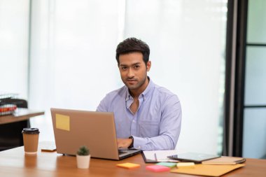 Ofiste dizüstü bilgisayarla çalışan genç Hintli bir adamın portresi.