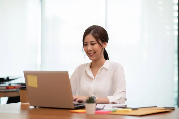 Happy Asian business woman working with laptop and smile looking at camera at modern office or Co-Working Space,Business Startup Concept