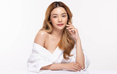 Bornoz giymiş güzel bir Asyalı kadın gülümsemesi yanaklarına temiz ve taze bir tene dokunur mutluluk ve neşe, olumlu duygusal, beyaz arka planda izole edilmiş güzellik kozmetik ve kaplıca konsepti.