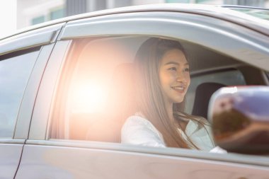 Güzel, çekici, genç bir kadın arabasında oturmuş gülümsüyor, kendinden emin ve mutlu bir şekilde dalan bir araba, mutlu ulaşım konsepti.