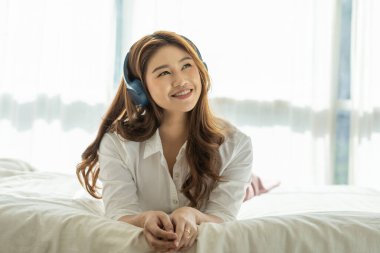 Güzel, çekici, Asyalı genç bir kadın müzik dinler ve yatak odasında uzanır. O yüzden rahatla ve rahatla, Seçici Odaklan.