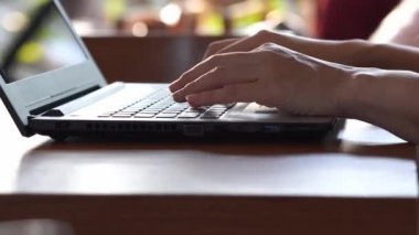 Beyaz tişört giyen, kahve dükkanında laptopla ve kahve bardağıyla çalışan iş kadınının ellerini kapat.