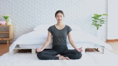 Çekici Asyalı kadın yoga nilüferine poz veriyor. Sabahları yatak odasında meditasyon yapıyor. Kendini çok rahat ve rahat hissediyor.