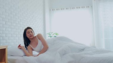 Yatakta uyandıktan sonra kolunu uzatan ve yatak odasındaki pencerelere bakan bir kadın sabah çok dinlenmiş ve rahatlamış hisseder, sağlık sigortası kavramı.