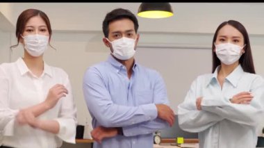 Maske takan Asyalı iş adamları, Covid-19 grip salgını ve korunması nedeniyle birlikte çalışma alanındaki iş ekibiyle karşılıklı güven içinde gülümsüyor. 