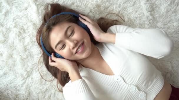 トップビュー美しい魅力的なアジアの若い女性は音楽を聞き とてもリラックスして快適なベッドルーム感覚でベッドの上に横たわっています 選択的フォーカス — ストック動画