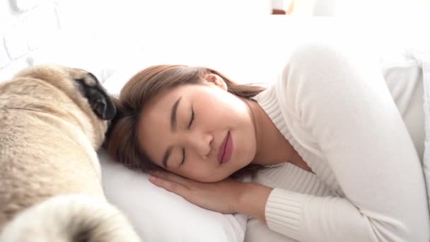 アジアの女性はPajamas睡眠を身に着けています彼女の目を閉じて笑顔睡眠と犬はとてもリラックスして快適な朝の感じで寝室で目覚めます ヘルスケアと睡眠の概念 — ストック動画
