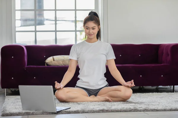 アスリートアジア系インド人女性のラップトップ練習ヨガ蓮のポーズ自宅でオンラインコースで瞑想快適でリラックスした ヨガ自宅で練習コンセプト Covid 19パンデミックによる自己分離 — ストック写真