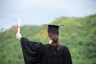 Mezuniyet kutlaması için elini kaldırdı. Virüs diploması ya da sertifikalı virüs salgını ve COVID-19 virüs gribi salgını için tıbbi maske taktı. Mezuniyet gününün yeni normu.