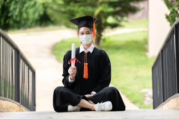 Graduated woman wear cap gown and  Medical mask for protection virus holding diploma or certificated due Virus outbrake and COVID-19 virus flu pandemic,New normal of graduation day