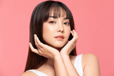 Güzel Asyalı kadın, yumuşak yanaklı gülümsemeye, temiz ve taze tenli mutluluğa, olumlu duygulara, pembe arka plana, güzellik kozmetiğine ve kaplıcaya dokunuyor.