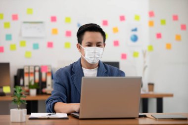 Modern ofiste dizüstü bilgisayarla çalışan Asyalı üst düzey iş adamı ya da Covid-19 Grip Salgını, Sağlık ve İş Kuruluşu Konsepti