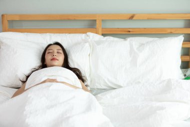Pijama giyen güzel Asyalı kadın gözlerini kapar gülümser ve tatlı rüyalar görür. Sabah yatak odasında uyur ve tatlı rüyalar görürüm. Rahatlayın ve rahatlayın, sağlık ve uyku konsepti.
