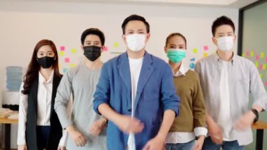Maske takan Asyalı iş adamları lideri grubu Covid-19 grip salgını ve korunması nedeniyle iş yerinde çalışan ekiple karşılıklı güven içinde gülümsüyor.