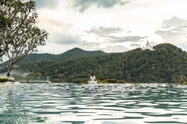 Güzel, çekici Asyalı kadının sakinliği sabah dağın zirvesinin üstündeki havuzda yoga nilüferinin pozunu pratik yaparken güzel doğa manzaraları karşısında çok rahat ve tatilde dinleniyor.