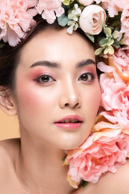 Kafasında büyük buket çiçekleri olan Asyalı güzel bir kadın. Temiz tenli, gülümseyen. Mutluluk ve neşe bej arka planda olumlu duygular, güzellik kozmetik ve yüz bakımı kavramları.