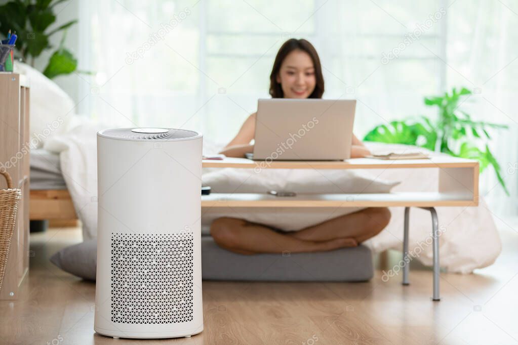 air purifier in living room for clean and fresh air with woman working with computer laptop and relax in background