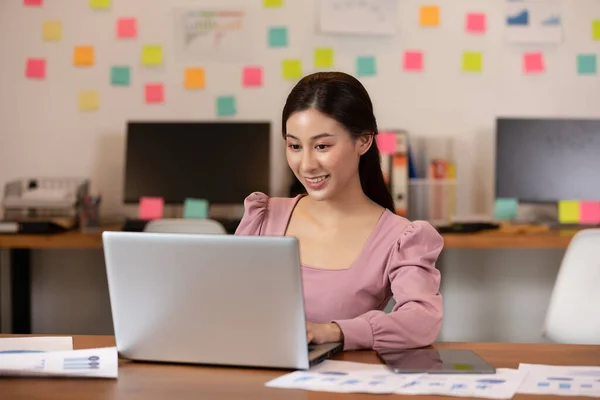 現代のオフィスやコワーキングスペースでカメラを見て ノートパソコンや笑顔でカジュアルな仕事をしている幸せなアジアのビジネス女性 ビジネススタートアップコンセプト — ストック写真
