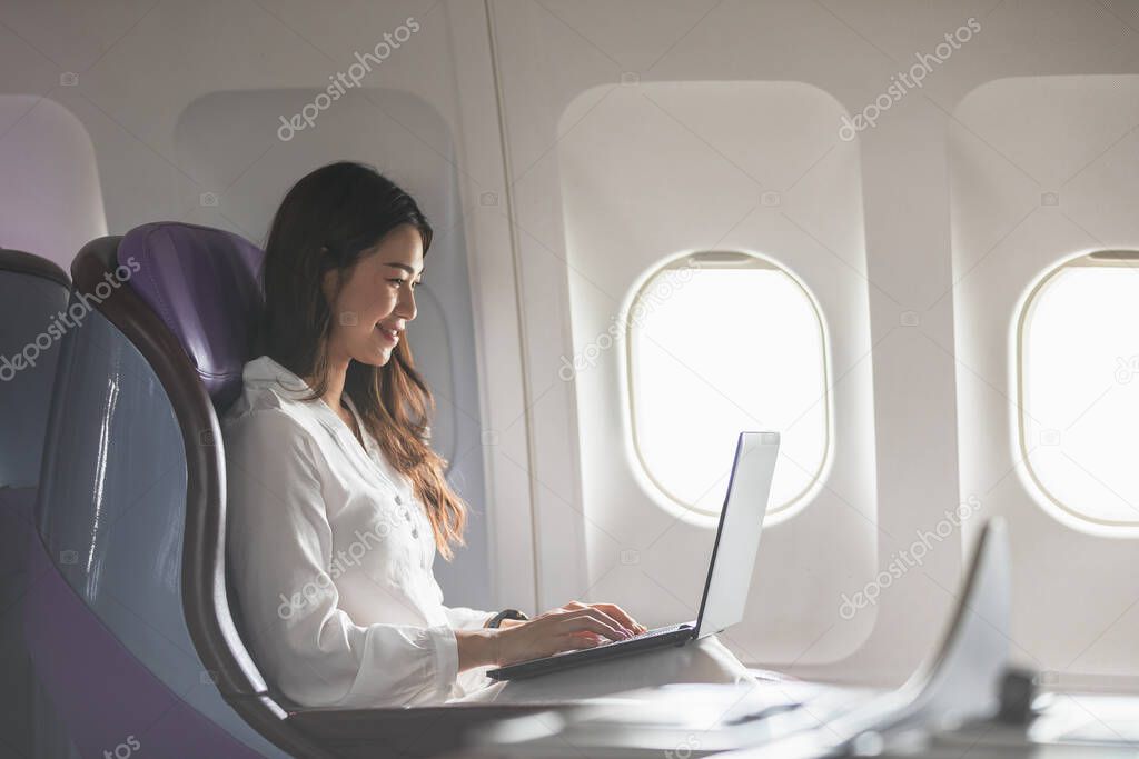 Asian young woman using laptop sitting near windows at first class on airplane during flight,Traveling and Business concept