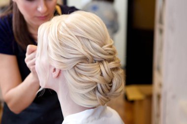 Makyaj sanatçısı genç ve güzel bir sarışın gelin için makyaj yapıyor. Güzel bir düğün gününde gelin mükemmel bir saç stiline sahip. Kuaförün becerisi sayesinde.