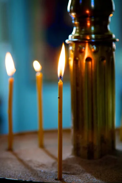 Three candles set in the sand burn and Shine. Golden radiance fills the atmosphere with calm and peace in the temple, faith hope and love are Church attributes