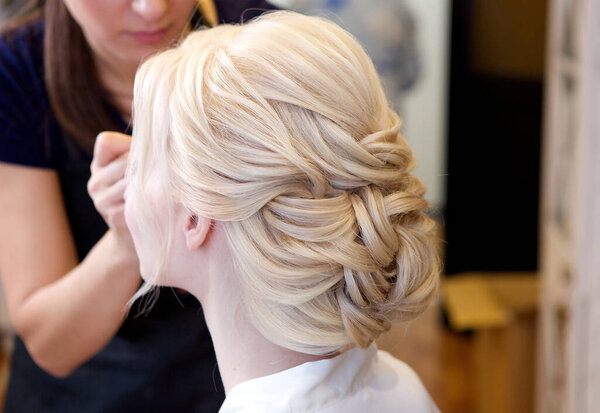 Make-up artist makes makeup for a young beautiful blonde bride. On a beautiful wedding day the bride has the perfect hairstyle thanks to the skill of the hairdresser