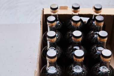 Tıpa kapaklı dolu cam şişeler karton bir kutuya konur. Şişedeki koyu sıvı, açık arkaplanda.