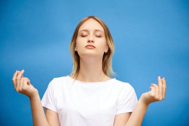 Genç sarışın güzel sarışın yoga yapıyor. Rahatlıyor ve mavi arka planda meditasyon yapıyor. Yoga konsepti, sağlık stresi rahatlaması..