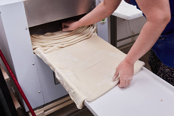 a female Baker works on an automated dough Forming machine in a bakery. culinary concepts manufacture of bakery products bread baking
