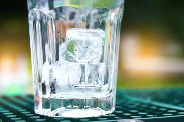 Transparent cold ice cubes in a transparent glass on a green table. Concept of outdoor recreation, preparation of a summer cooling cocktail, ice, frost