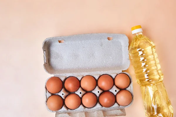 10 eggs in a cardboard egg box and a bottle of sunflower oil on a light, simple table. Brown fresh eggs cooking concept, in the kitchen, grocery store, close-up isolated
