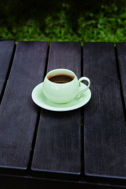 Sıcak bir yaz gününde, siyah ahşap bir masada bir fincan kahve. Masa yeşil çimlerin üzerinde, yakın plan.