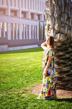 Geleneksel makyajsız, genç ve güzel bir Hintli kız bir yaz akşamı palmiye ağacının yanında duruyor. Güneşin parlak ışınlarının altında, temiz havada. Hintli genç güzel kız model..