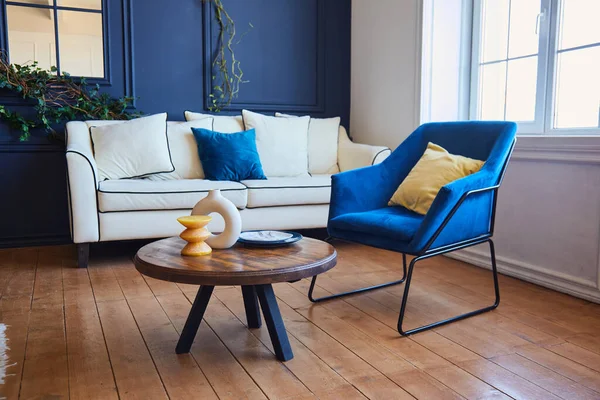 Geniş, mavi duvarları, ahşap zemini, mavi koltuğu ve beyaz koltuğu olan modern bir oturma odası. Sanat konsepti Nouveau tarzı, gerçek bir iç mekan fotoğrafı..