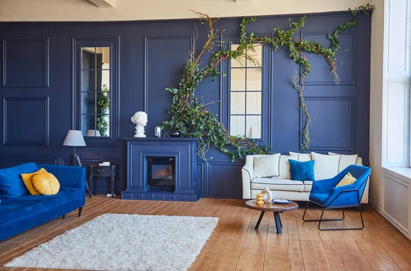 Şömineli, mavi duvarlı, ahşap zeminli, parlak sarı yastıklı, mavi koltuklu, ferah oturma odası. Yerde beyaz halı var. İçinin gerçek bir fotoğrafı..