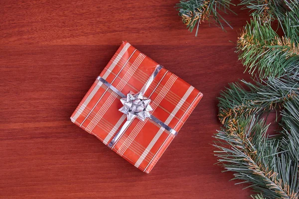 Çerçeve, merkezdeki ahşap bir masanın üzerinde yeşil dalları olan kozalaklı ağaçlardan yapılmış bir hediye kutusu. Yeni yıl kavramı, Noel 'in aile tatilini kutlamak. Yatay fotoğraf