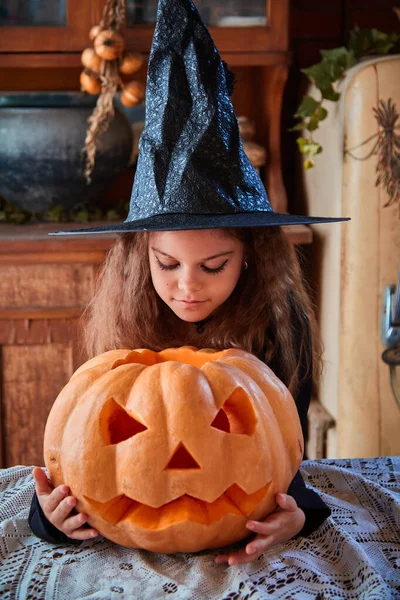 Cute girl aged 9 years old in a witch costume in an old house for Halloween with a pumpkin. The concept of witchcraft, evil spirits and a fabulous autumn holiday Halloween