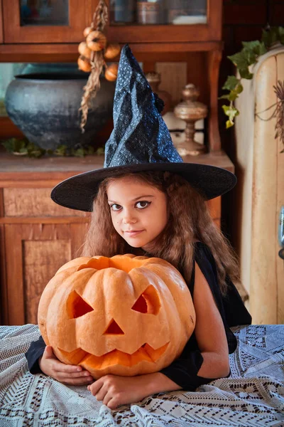 Cute girl aged 9 years old in a witch costume in an old house for Halloween with a pumpkin. The concept of witchcraft, evil spirits and a fabulous autumn holiday Halloween