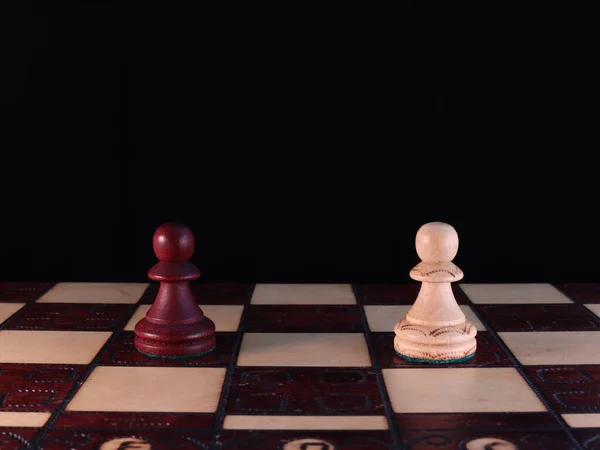 İki el yapımı, ahşap, satranç figürü satranç tahtasının üzerinde duruyor..