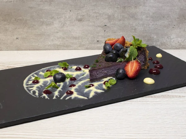 Creative serving of blueberry pie on slate. The cake is decorated with strawberries, blueberries and a cream tree with mint leaves.