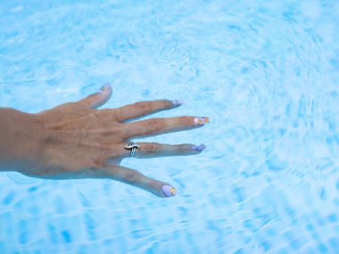 Genç bayan parmaklarını jöle tırnaklarıyla havuza daldırıyor..