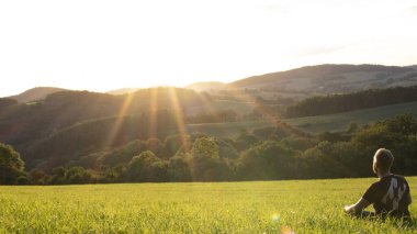 Gün batımında çayırda oturan genç bir adam.