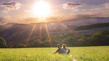 Gün batımında çayırda oturan genç bir çift.