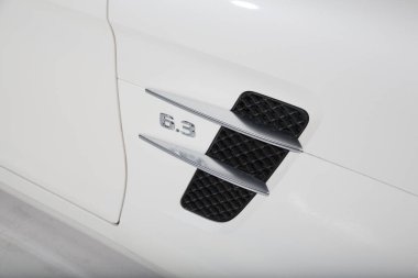 Beyaz bir Mercedes AMG arabanın yanında motor büyüklüğünde logo var.